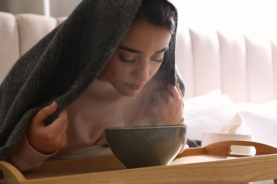young woman leaning over steaming bowl with towel over her head
