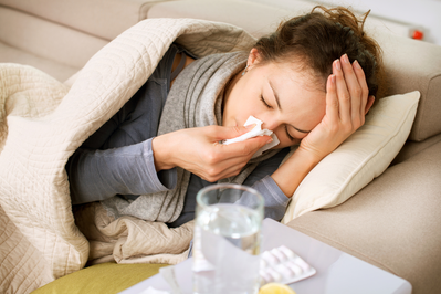 sick woman lying on couch blowing nose