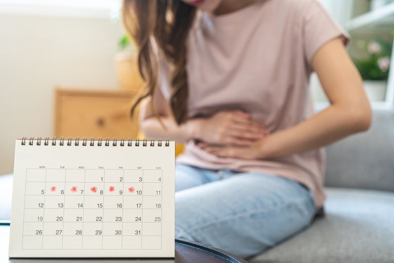 girl with PMS holding abdomen next to calendar showing period dates